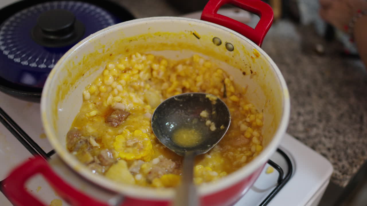 Simmering pot of golden locro reveals tender pumpkin, yellow corn kernels and slices of chorizo in rich broth, steam rising as ladle dips into the thick Argentine stew in cozy home kitchen slow motion