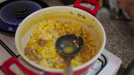 simmering pot of golden locro reveals tender pumpkin, yellow corn kernels and slices of chorizo in rich broth, steam rising as ladle dips into the thick argentine stew in cozy home kitchen slow motion