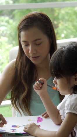 a young, asian child work and play at home with her mother learning to read and write in the cozy comfort of their living room