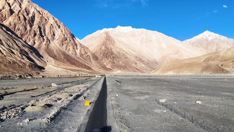aerial drone shot following a car along a serpentine road cutting through ladakh's stark landscape.