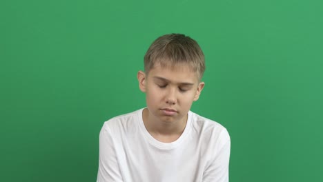 upset disappointed depressed teenage boy sitting lowered his head, raises and lowers his head sadly. emotions, problems, depression. green screen chroma key background. 4k video