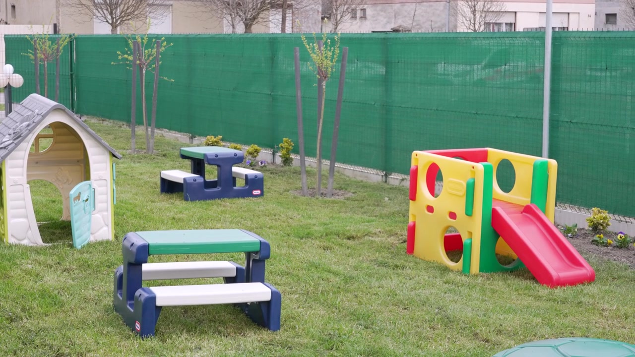 Parque infantil colorido com escorregadores e mesas de plástico à espera de crianças em um quintal gramado.