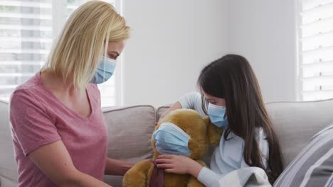 girl putting face mask on her teddy bear toy at home