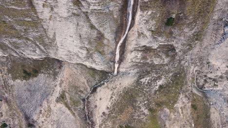aerial slow-motion top down flying up over a high thin waterfall in tzoumerka, greece