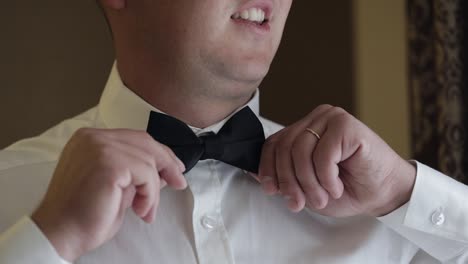 Groom-man-adjusts-bow-tie,-preparing-to-go-to-the-bride,-businessman-in-white-shirt,-wedding-day