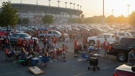 vibrant atmosphere of a tailgate party with enthusiastic fans gathered in a parking lot, celebrating and preparing for an exciting game ahead amidst vehicles and sunset