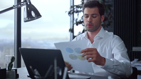 Businessman-having-video-call-on-laptop-in-office.-Man-looking-at-graphs