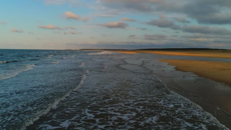 Un-Dron-Aéreo-Bajo-Disparó-A-La-Hora-Dorada-Sobre-Pequeñas-Olas-Rompiendo-La-Costa-De-La-Playa-De-Arena-Con-Arena-Dorada-En-El-Reino-Unido