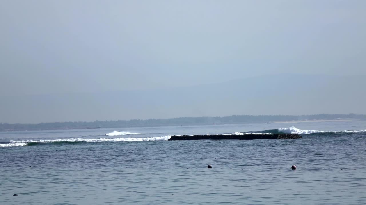 따뜻한 바다의 파도는 우산과 셰이즈 라운지와 함께 열대 휴양지의 모래 해변에 달립니다.