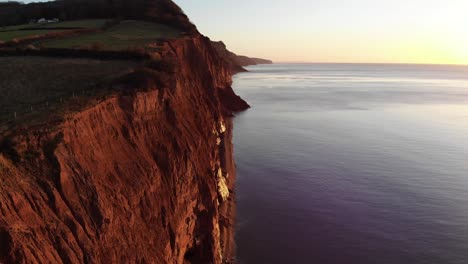 aéreo a lo largo de los acantilados de la costa de sidmouth bañados por la luz dorada del amanecer en la mañana