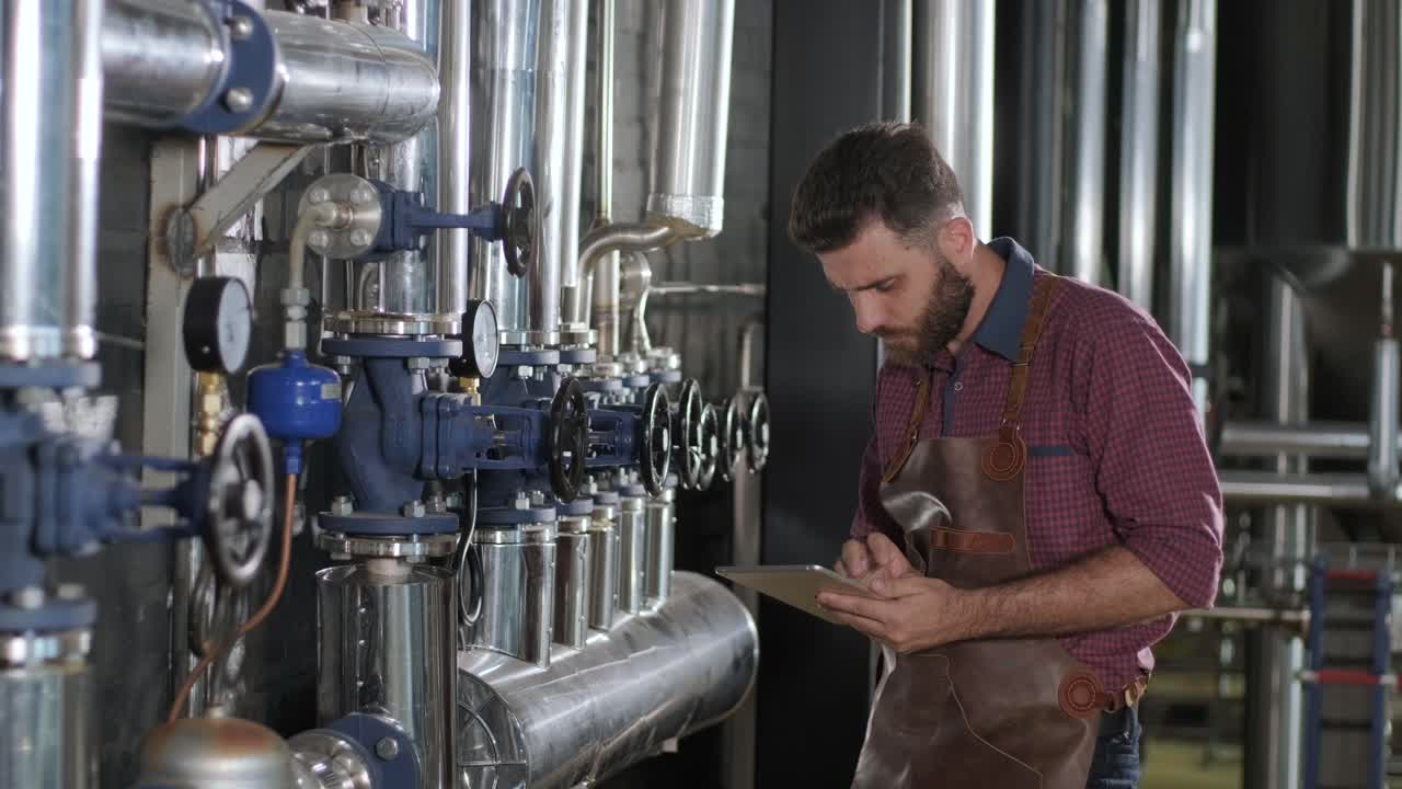 un joven cervecero con un delantal de cuero supervisa el proceso de fermentación de la cerveza en una fábrica de cerveza moderna