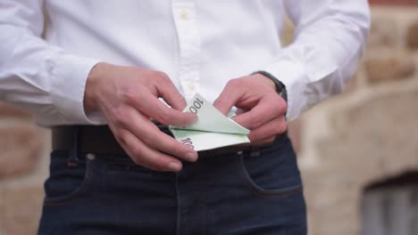 young businessman counting one hundred euro banknotes in his hands and putting them back in his pocket