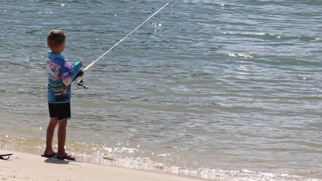 un niño disfruta pescando solo en una playa soleada