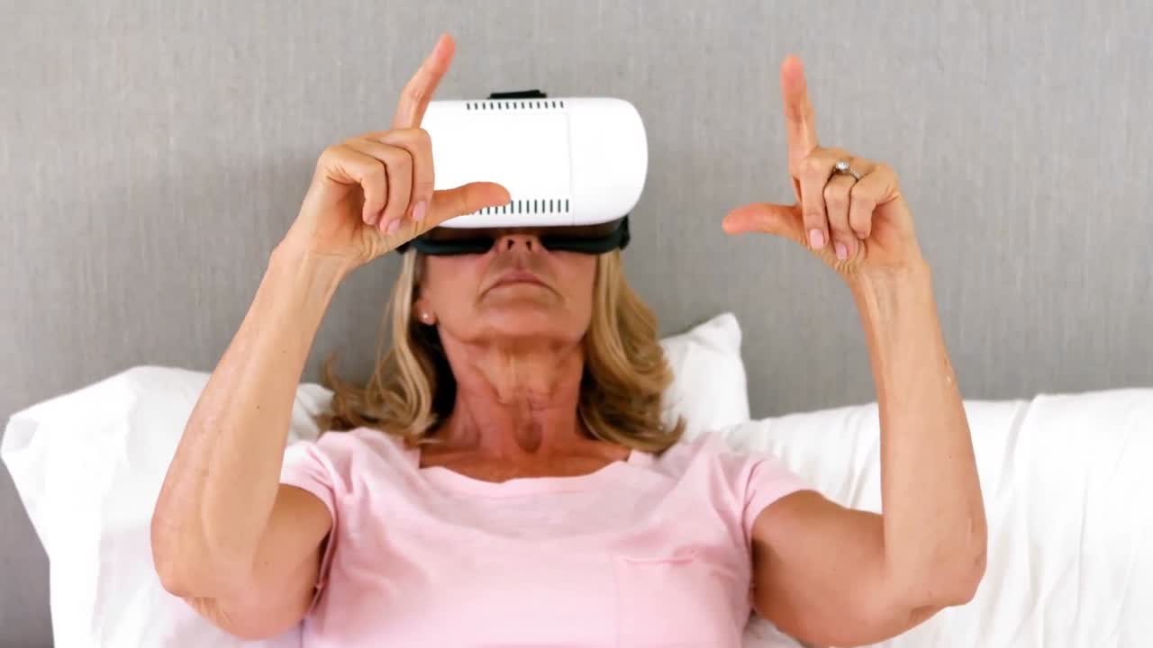 mujer mayor usando auriculares de realidad virtual en la cama en el dormitorio