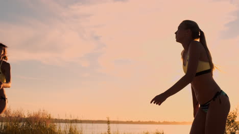 movimento lento baixo ângulo close up lente flare: jovens jogadoras de voleibol passam e espetam a bola sobre a rede em uma noite de verão ensolarado. fit meninas caucasianas jogando voleibol de praia ao pôr do sol.