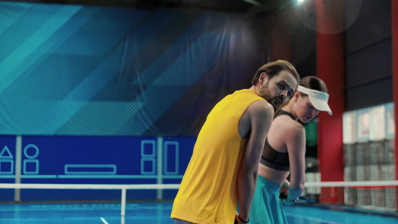 Mężczyzna uczy kobietę grać w pickleball na korcie wewnętrznym