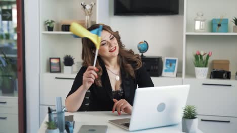 the woman is sitting at a desk in an office, waving the flag of ukraine in front of her laptop camera