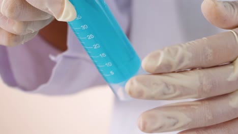 close-up of gloved hands carefully holding a test tube filled with blue liquid.