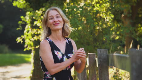 portrait of casually dressed mature woman leaning on fence on walk in countryside