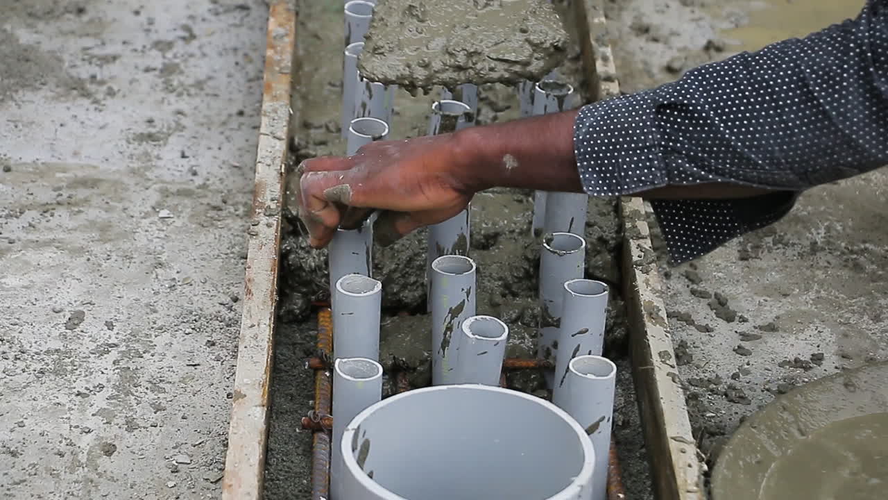 Indian mason worker placing concrete wet mix around pipes to level a slab for construction work.