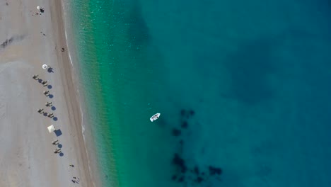 Paradiesischer-Sandstrand-Mit-Sonnenschirmen-Und-Sonnenliegen,-Die-Von-Ruhigem,-Klarem-Wasser-Des-Türkisblauen-Meeres-Umspült-Werden