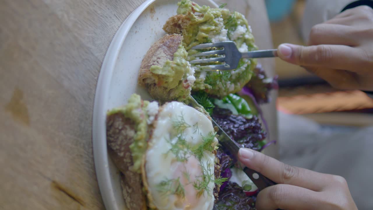 Person eating avocado toast with a fried egg for breakfast