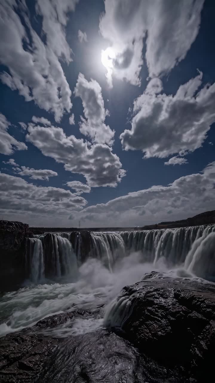 Dramatic low-angle shot of a waterfall under a cloudy sky, capturing the motion and power