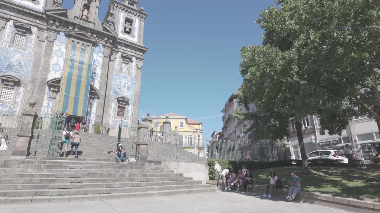People walking through Praça da Batalha in Porto on a sunny day, market stalls line the square