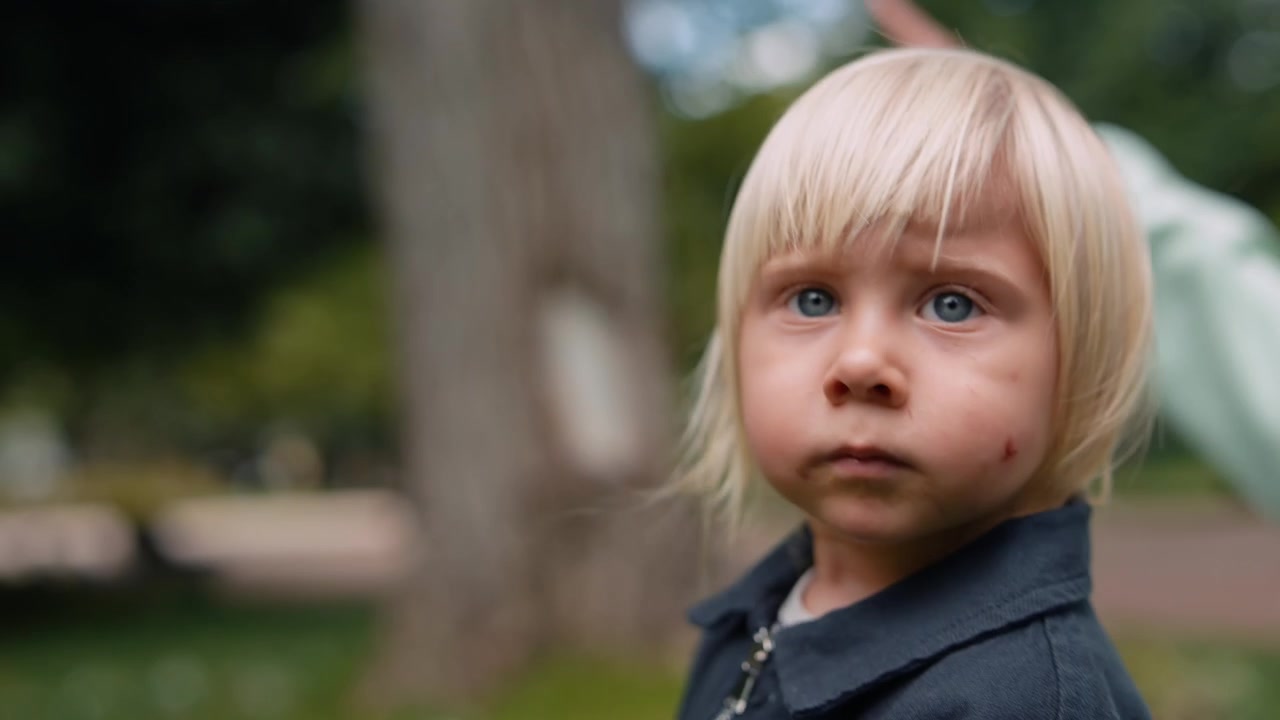 Bambin blond aux yeux bleus avec une égratignure sur la joue, regardant l'appareil photo