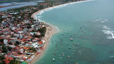 rising tilting up aerial drone wide shot of the porto de galinhas or chicken port beach with anchored sailboats and tourists swimming in the crystal clear ocean water in pernambuco, brazil