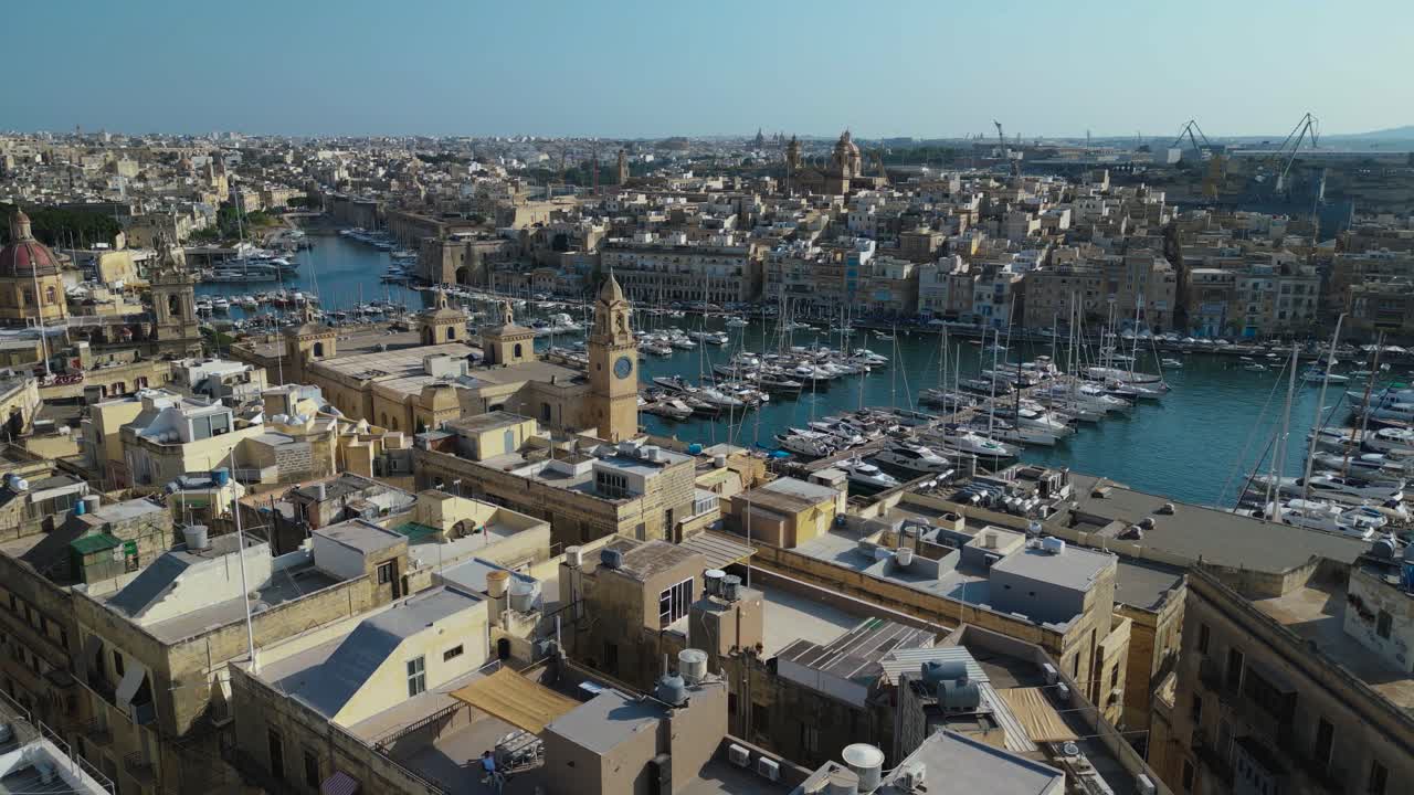 Vista aerea di Birgu, Malta, che mostra le strade storiche, le fortificazioni e il vivace porto. Edifici in pietra calcarea e costa mediterranea ripresi dall'alto