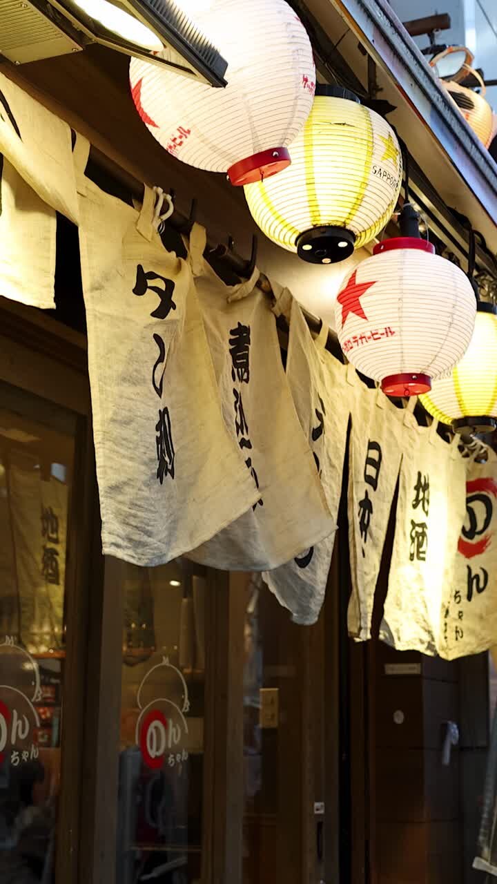 Inquadratura dal basso di lanterne di carta illuminate e tende di tessuto fuori da un ristorante di Tokyo