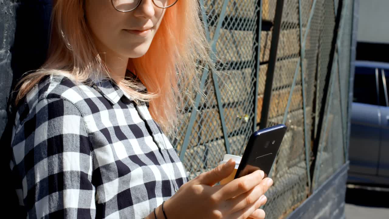 Donna che usa il cellulare appoggiata al muro in una giornata di sole 4k