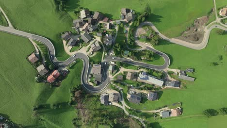 an overhead aerial tilt down view of cars moving on a winding road of the small village of la val, south tyrol, italy with it's lush green steep grass covered hills