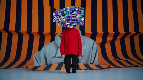 fashion model is posing wearing red sweater and black pants with multiple eyes collage on head in front of giant eye painting and orange and dark blue striped background