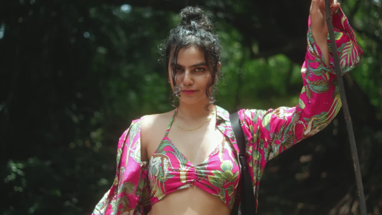 Mulher elegante com blusa tropical vibrante posa na floresta com expressão confiante
