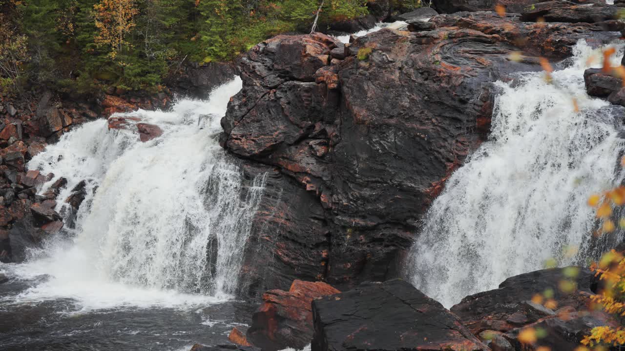 En rolig foss fosser over mørke steiner, dens milde strøm harmoniserer med den fredelige atmosfæren i det bortgjemte skogsområdet