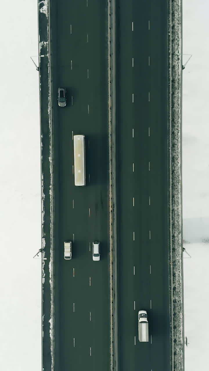 wide black highway bridge with fast moving vehicles over white snowy and icy frozen river surface bird eye view