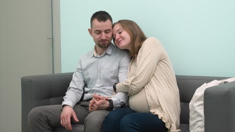 Loving-Pregnant-Couple-Sitting-In-Waiting-Room-For-A-Gynecological-Consultation