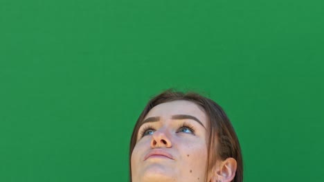 static close-up shot of a brunette lady's face from the nose up in front of a green chroma key backdrop looking at the sky with excitement and laughter