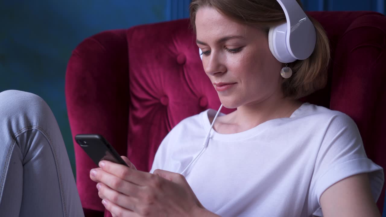 una joven sonriente escuchando música mientras está sentada en un sillón