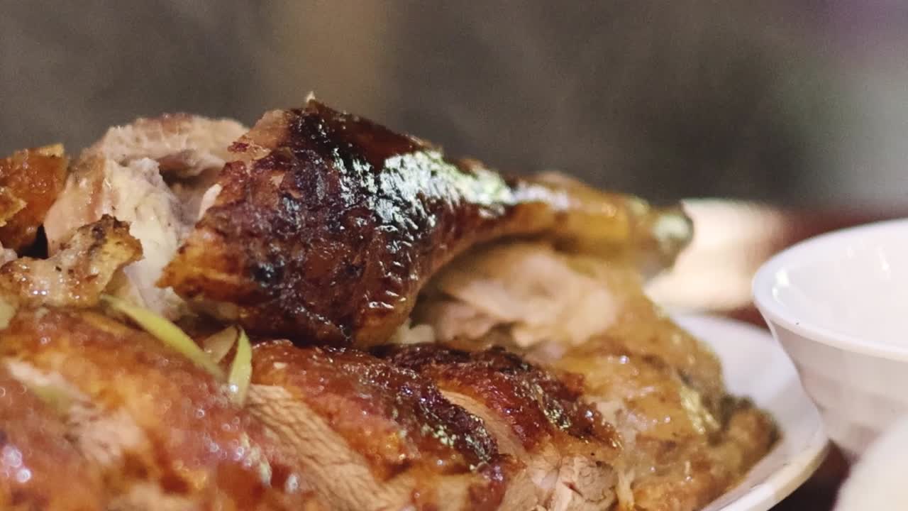 Detailed view of succulent roasted duck with crispy skin, served alongside a small bowl of sauce.