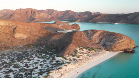 Filmische-Drohnenaufnahme-Des-Strandes-Von-Balandra,-Vorbei-An-Den-Roten-Hügeln-Und-Dem-Türkisfarbenen-Wasser