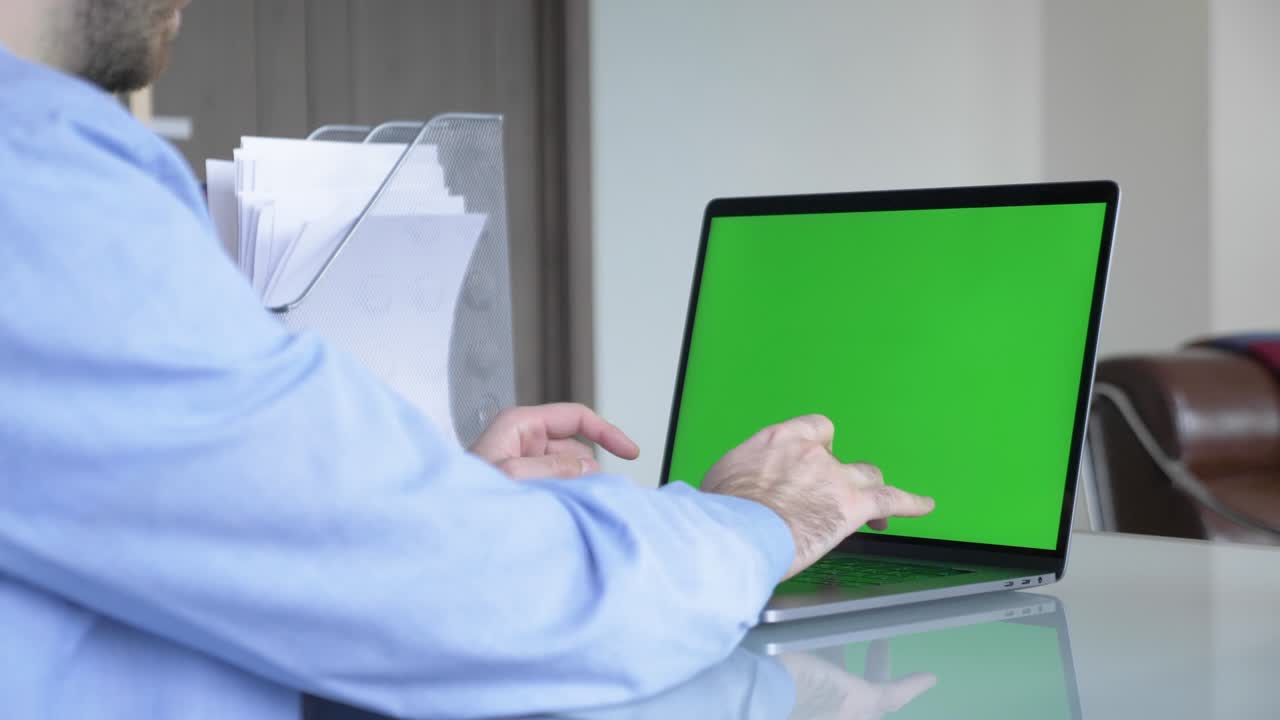 hombre en la oficina de casa escribiendo en el teclado de la computadora portátil con una maqueta de croma de pantalla verde