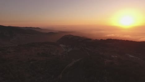 stunning high aerial view above mountain range and clouds toward bright yellow sunset