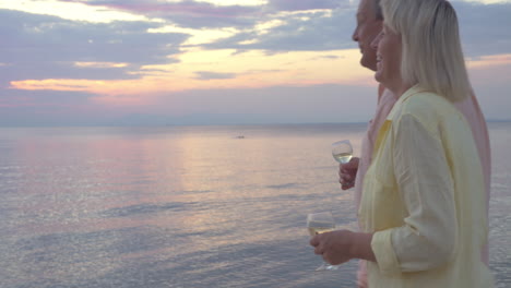 mature couple with wine glasses walking by the sea