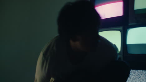 young alternative boy sitting alone in the dark room with vintage crt tvs, standing up and leaving after a mental crisis