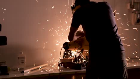 Hombre-En-Cuarto-Oscuro-Corta-Con-Sierra-Eléctrica,-Saltan-Chispas,-Tiro-Medio-Tira-Hacia-Atrás