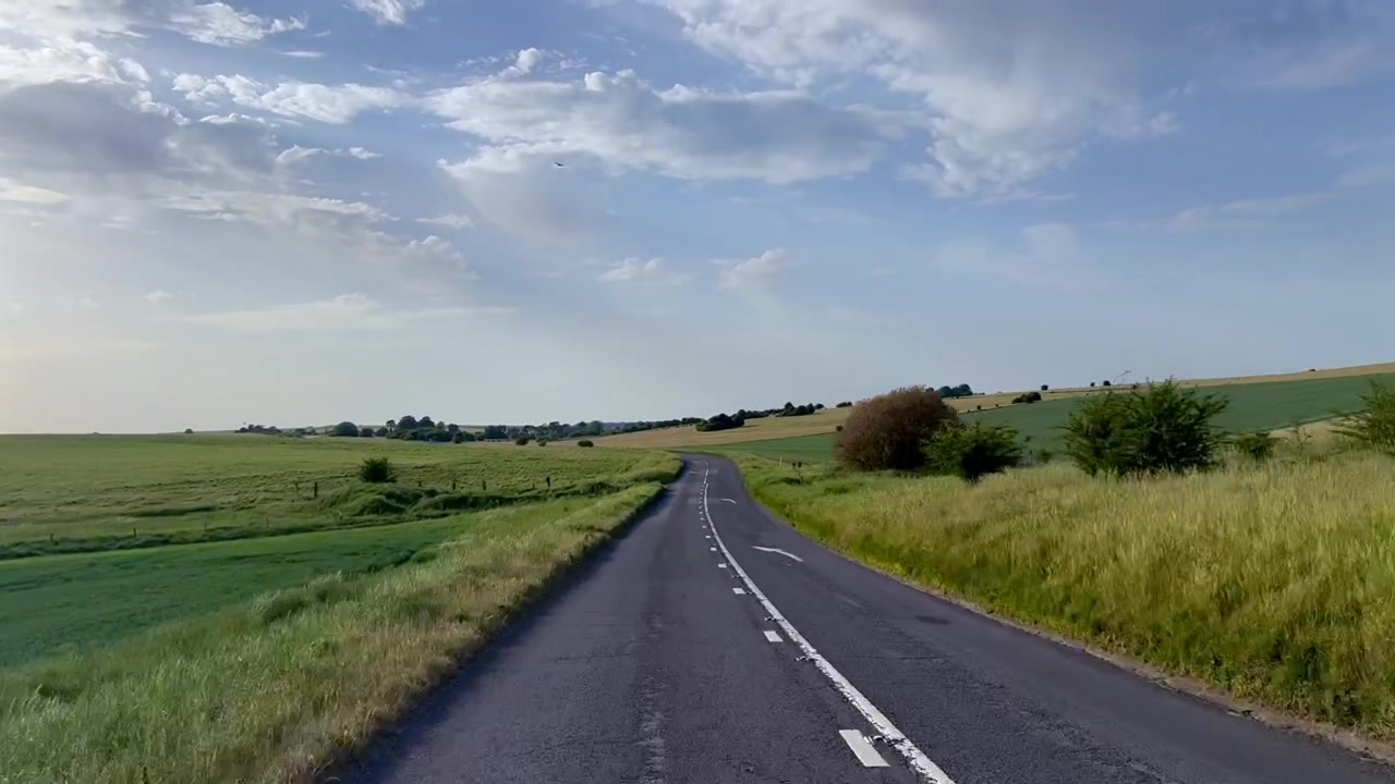 Bil POV kører gennem åbent, britisk landskab en sommeraften.