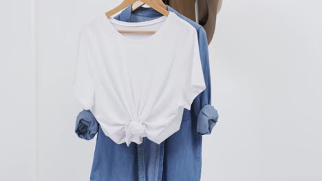 Video-of-white-and-denim-t-shirt-on-hangers,-hat-and-copy-space-on-white-background